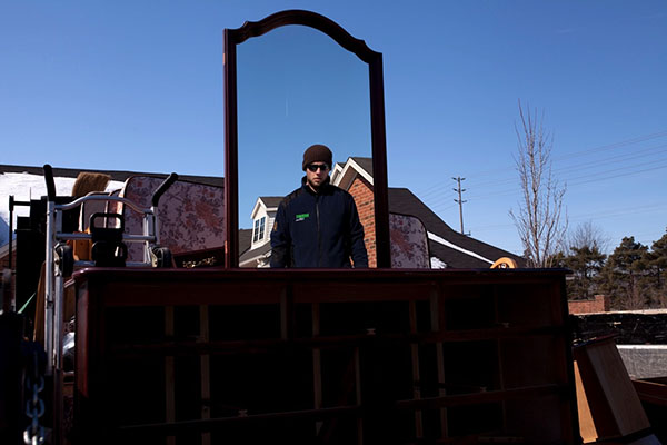 A man is looking into a mirror as he is moving several items of furniture